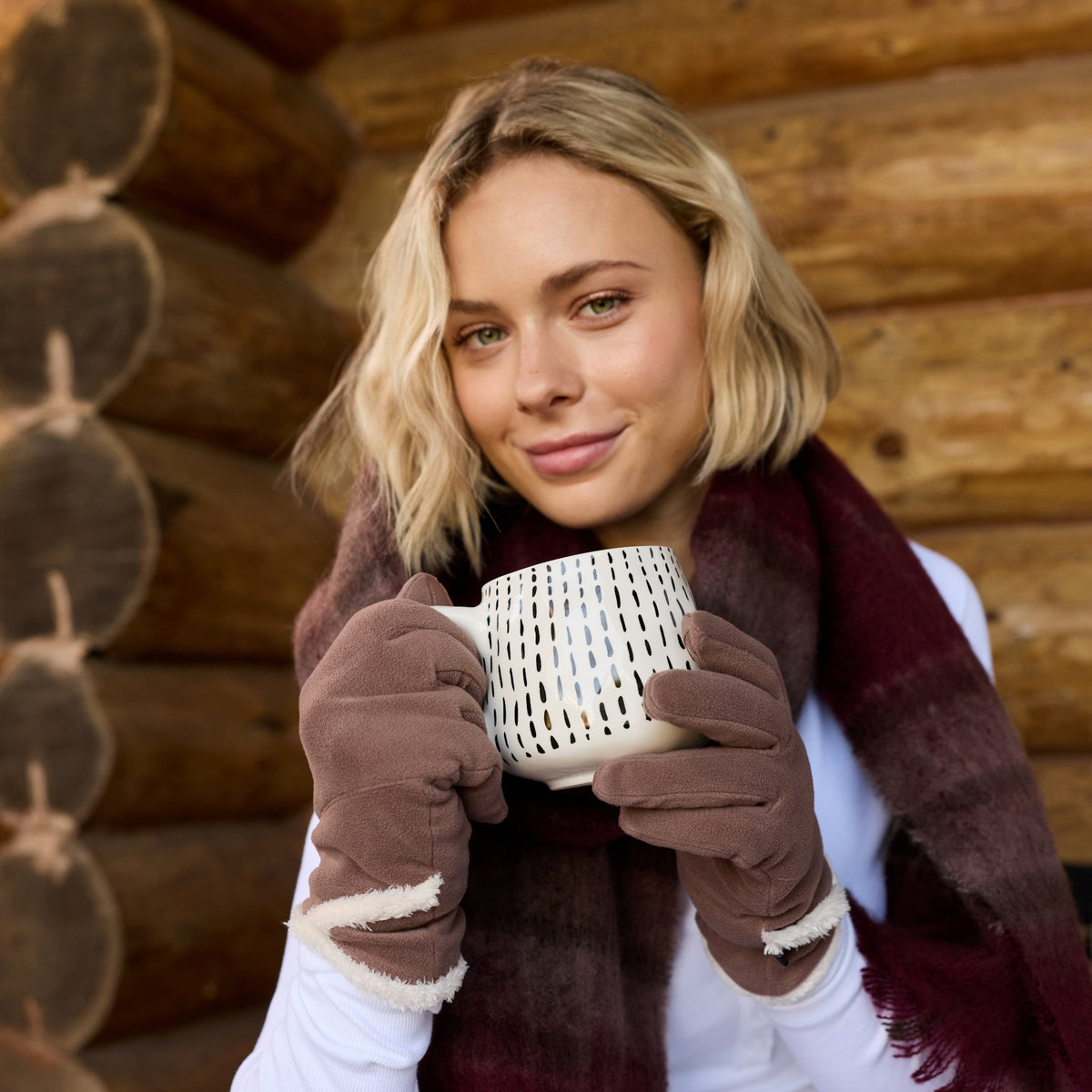 A woman wearing a gray blazer, white top, and a dark burgundy plaid scarf sits on a wooden porch next to a log cabin wall.

#color_cheetah