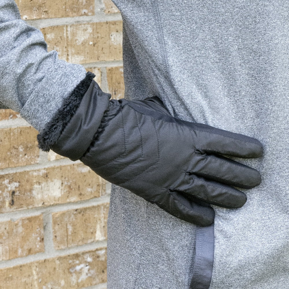 Women’s SleekHeat™ Quilted Gloves in Black on figure. Model wearing performance clothing with her gloved hand on her hip against a brick wall