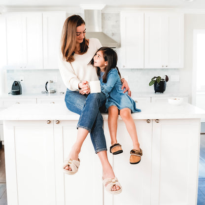 Signature Women’s Microterry with Satin X-Slide Slippers on figure. Mom wearing the x-slides, holding a cup of coffee and snuggling her daughter who sits next to her on the kitchen counter