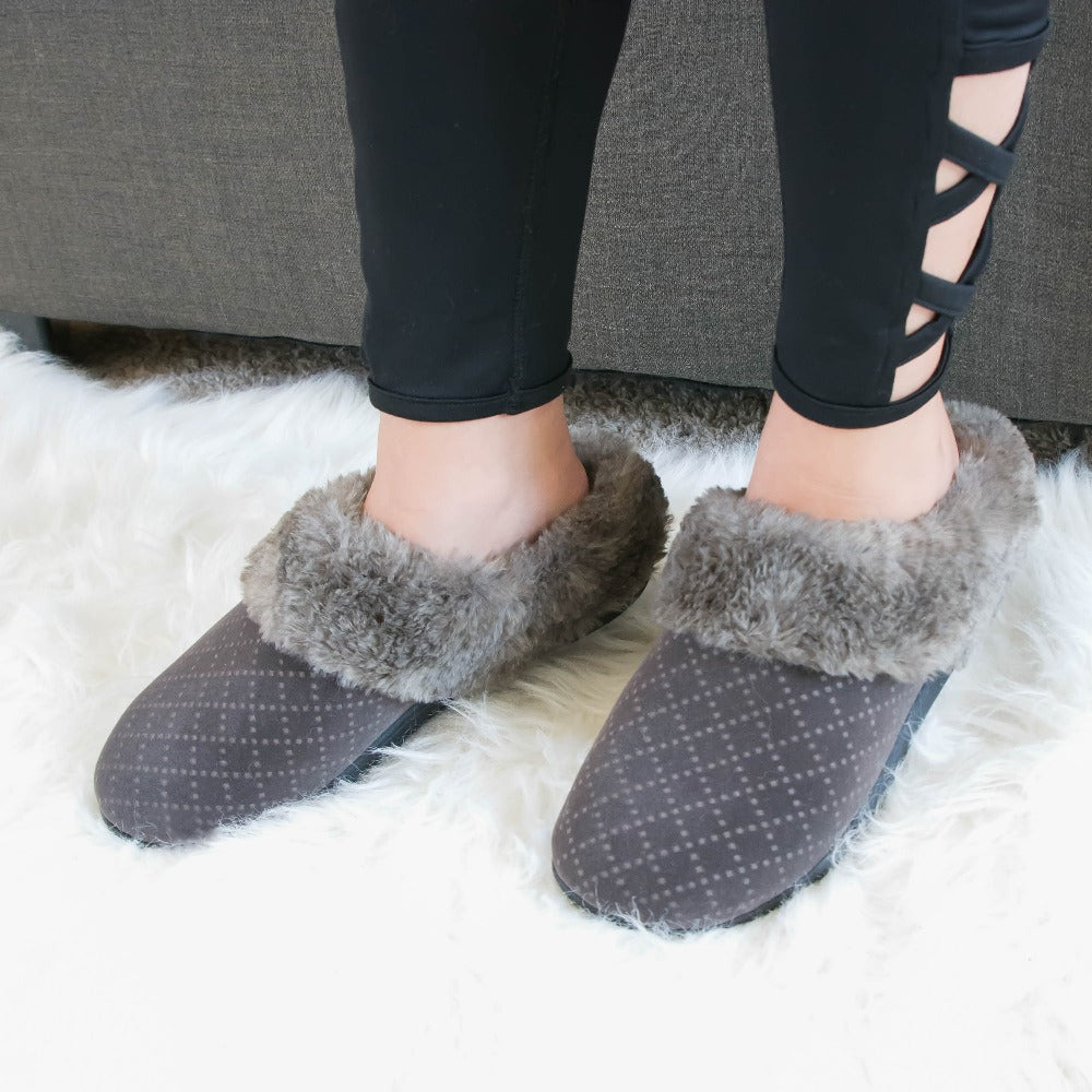 Women’s Velour Sabrine Hoodback Slippers in Mineral on figure sitting on a couch with her feet on a fluffy rug