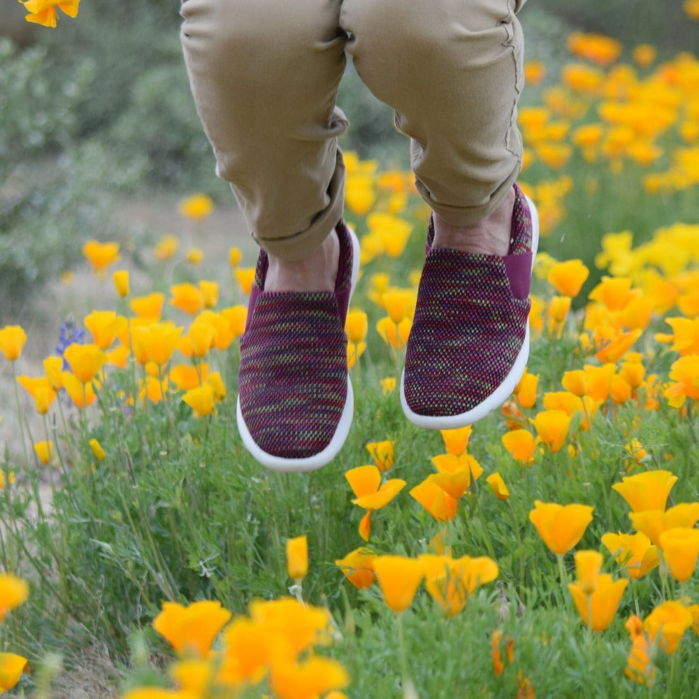 Woman jumping in a field of poppy flowers wearing the zenz balance slip on